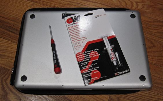 A screwdriver and conductive grease resting on the back of a laptop