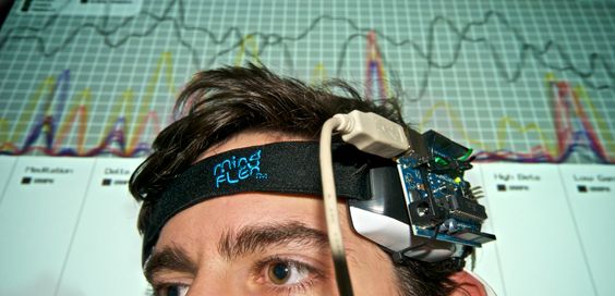 A person wearing a hacked MindFlex EEG headset in front of a projection of its data visualization